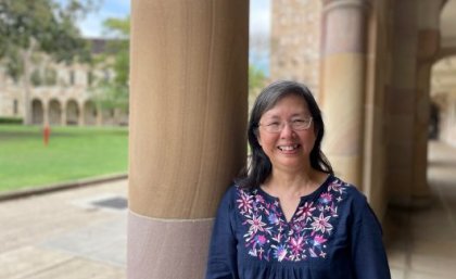 Dr Poh Hillock standing outside a sandstone building with trees behind her.